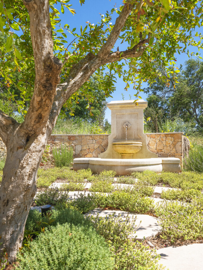 Fontaine en pierre adossée à un muret en pierre, dans un projet paysager signé Adonis Paysages