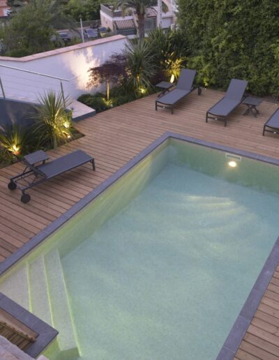 Renovated pool with wooden deck, loungers and modern landscape lighting
