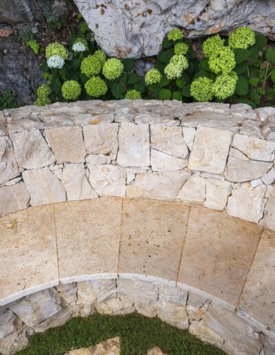 Banc en pierre aménagé contre une restanque, entouré d’hortensias et de rochers naturels