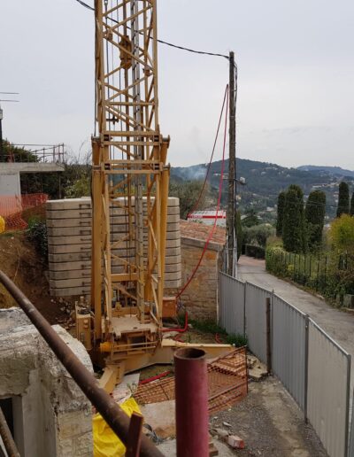 Travaux de construction d’un muret en pierre avec grue sur un terrain en pente.
