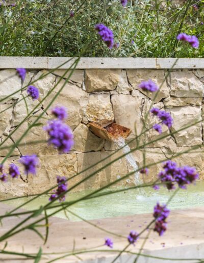 Gros plan sur le bassin en pierre et les reflets de l’eau dans le jardin de la villa Hinn