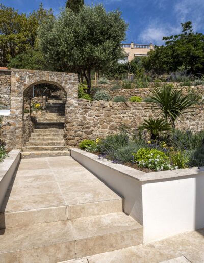 Escalier sous voûte en pierre donnant sur un jardin méditerranéen en restanques