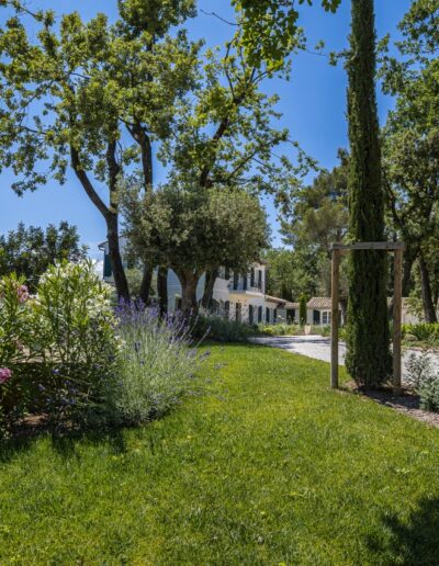 Flower beds and green lawn along a path leading to a Provençal house