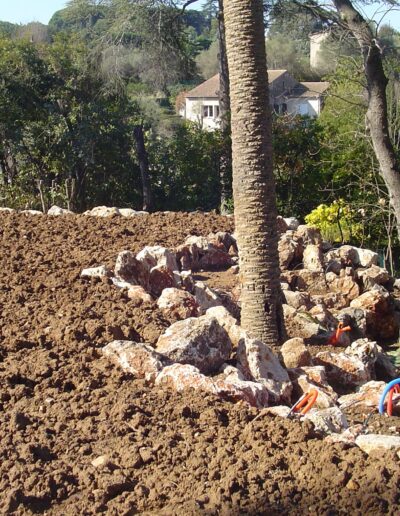 View of a landscaping worksite with turned soil, rock formations and palm trees