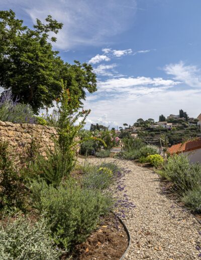 Gravel pathway lined with Mediterranean planting and a stone wall overlooking the hillside