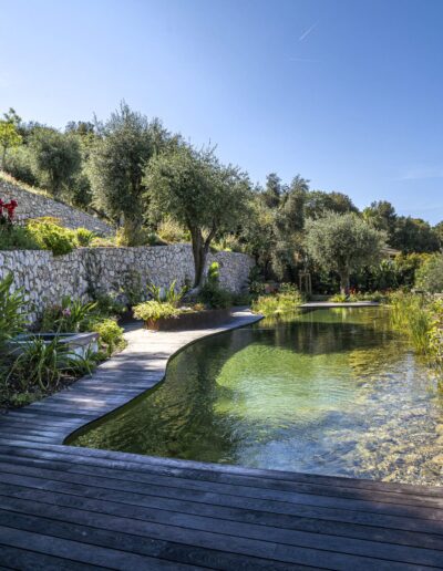 Clear-water natural pool with wooden decking and dry-stone walls in a Mediterranean garden