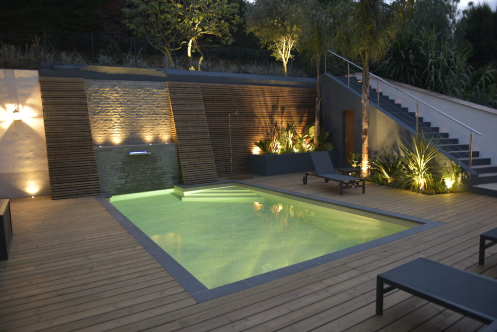 Terrasse en bois avec piscine, de nuit, plantes éclairées par le dessous, ambiance cozy