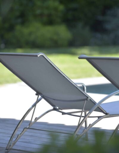 Two modern sun loungers set on a wooden deck beside a pool