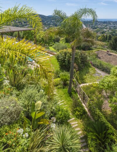 Pedestrian passage surrounded by Mediterranean plants and a dry-stone wall.