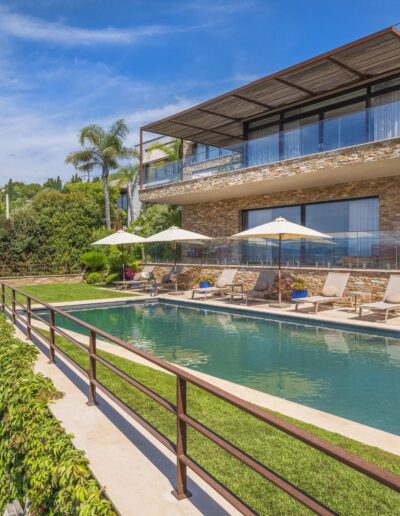 Vue du jardin paysagé avec piscine et grande terrasse en pierre dans une villa contemporaine à Mougins.