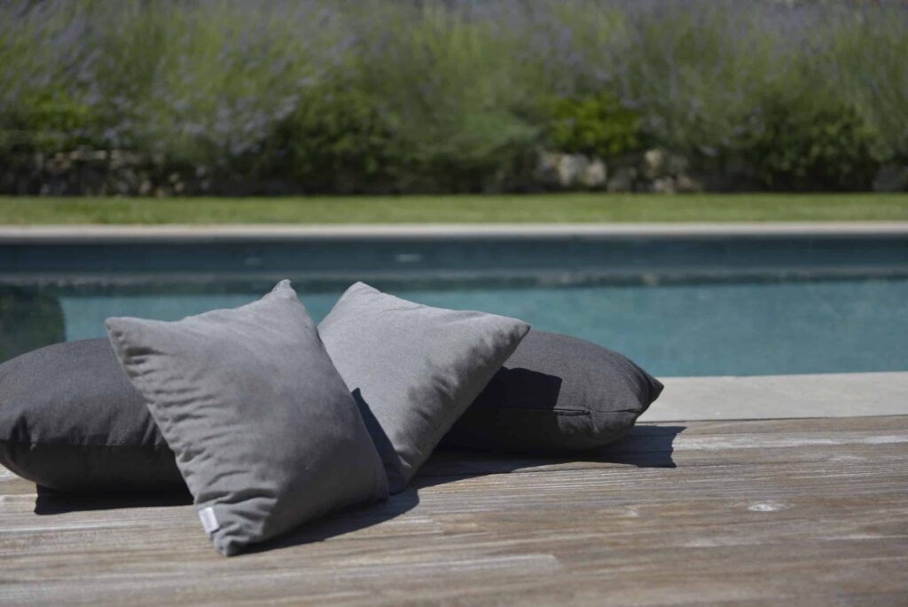 Outdoor cushions arranged on a wooden terrace in front of a pool