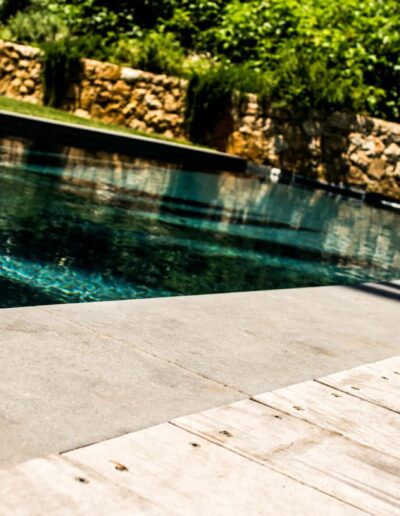 Close-up of the pool edge with stone coping and wooden deck, featuring turquoise water