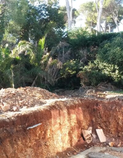 Pool excavation work showing a large soil cut at the base of a densely vegetated embankment