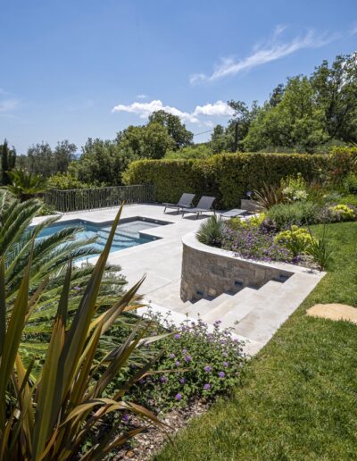 Swimming pool surrounded by Mediterranean vegetation, stone terrace and flower beds