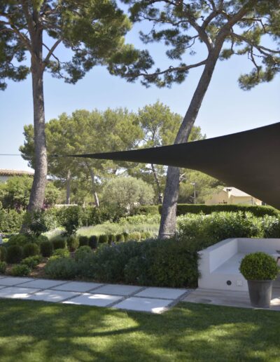 Shade sail stretched between tall pine trees above a landscaped garden with a stepping-stone path