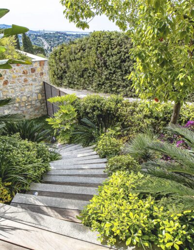 Wood and stone garden staircase lined with lush plants with a view over the bay