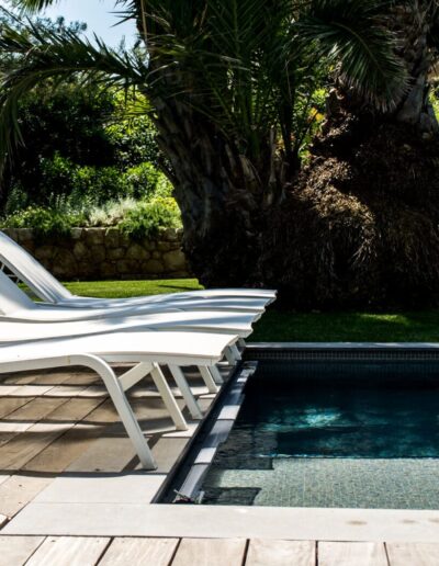 Row of white sunbeds beside a pool surrounded by Mediterranean vegetation