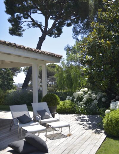 Wooden deck with two white loungers and grey cushions, surrounded by white hydrangeas and Mediterranean garden plants